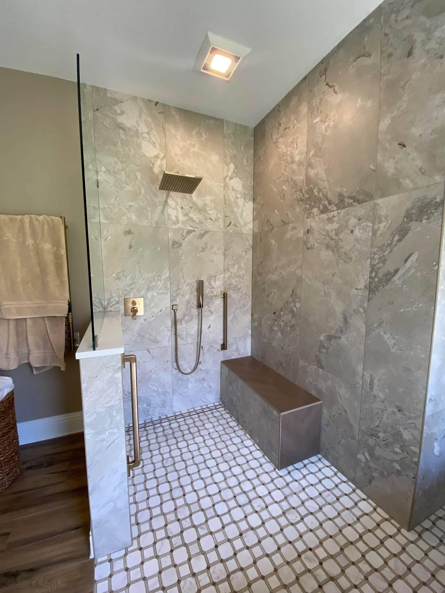 Walk-in shower in large format marble-look tile with a brass rain head, a handheld on a rail, a grab bar, a built-in bench finished in chevron tile and an octagon mosaic floor