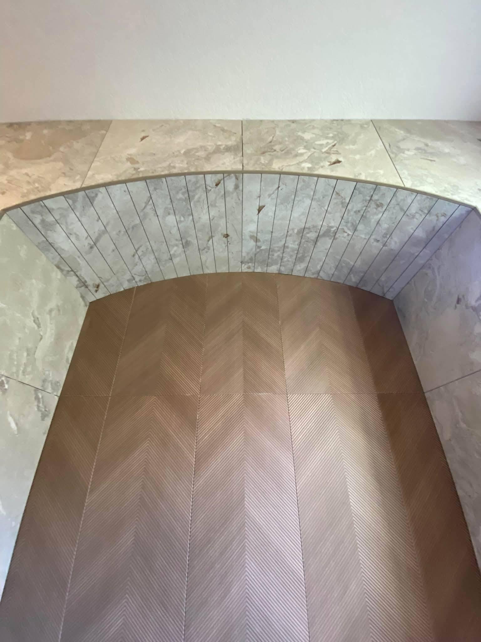 Close view of the arched opening, with the marble-look tile cut into tapered voussoirs that follow the curve and meet a chevron-textured panel below